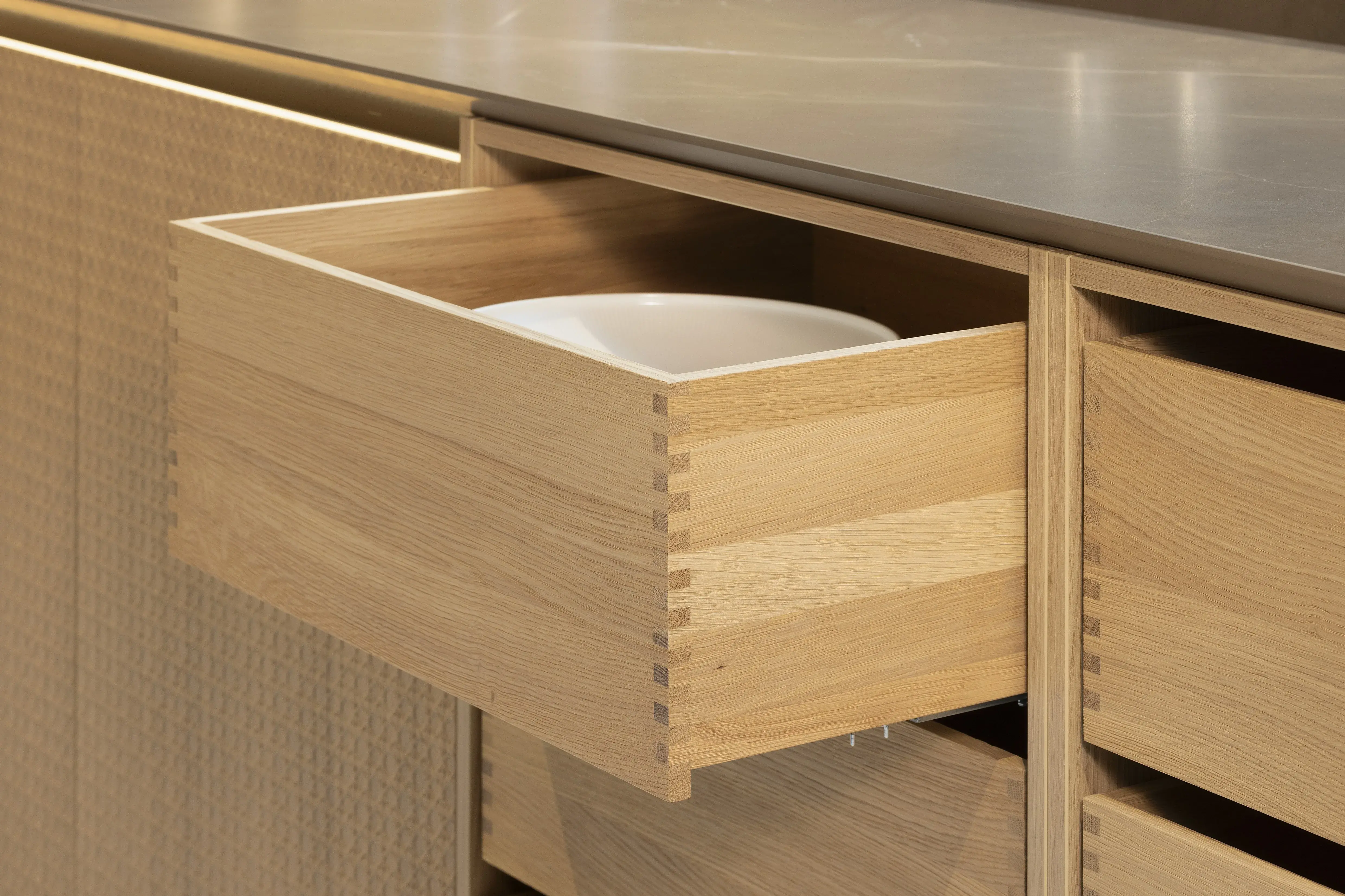 APL: Pulpis (Keramik) 25 mm Front: AV 6085-GL Eiche-elegant Echtholzfurnier (PURemission) Korpus: 2085 Designkorpus Feineiche-natur Griff: Kehlleiste 355 Schwarz matt Geräte: Siemens  Armatur: Gessi Spüle: ?  Features: neue Oberfläche Wiener Geflecht in Echtholzfurnier, Oberflächenmix, Waschbecken (Spülstein) in APL-Material, schwebende Arbeitsplatte durch Lichtleiste, APL abgekantet (schwebend), Backöfen in Wand eingekoffert, 3 Materialfarben.