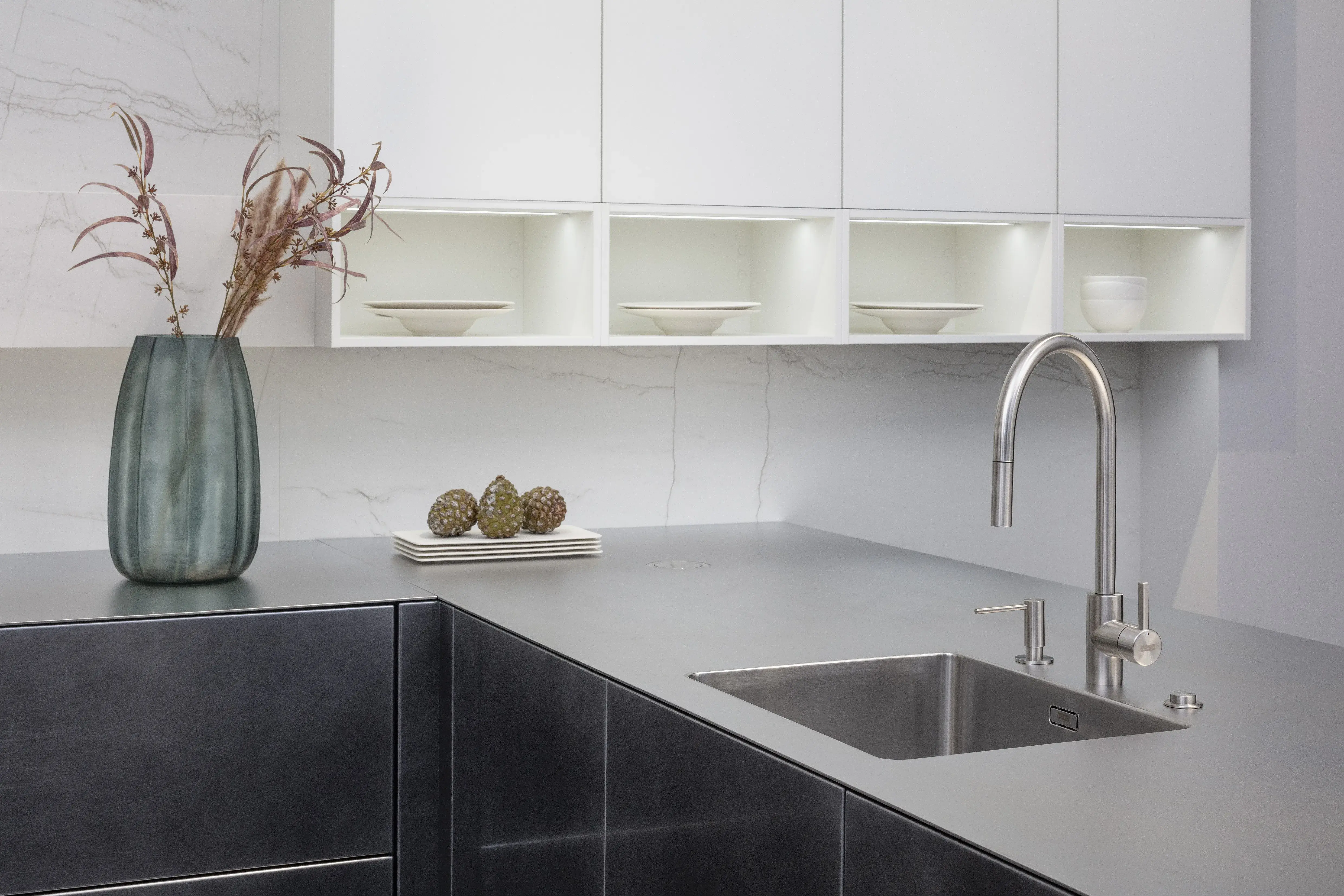 Front: Industriestahl Metalliclack geschliffen AV6000 NCS Mattlack APL: Franke Edelstahl 6 mm Geräte: Bora Spüle Armaturen: Franke  Features: Metallfront, Spülbecken in APL integriert (aus einem Guss), Oberschränke mit Lowboard-Charakter, integrierter Arbeitsplatz, dunkler Korpus mit Aluminium-Abschlussleiste, Wärmeschublade mit Gittereinsatz.